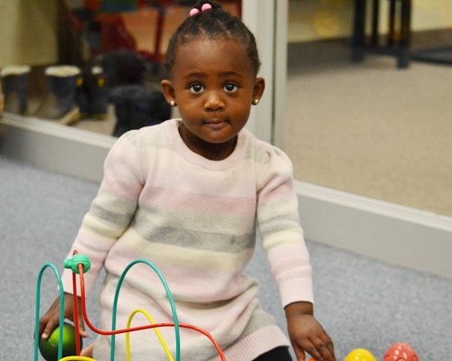 A child playing with toys while looking at the camera and smiling slightly