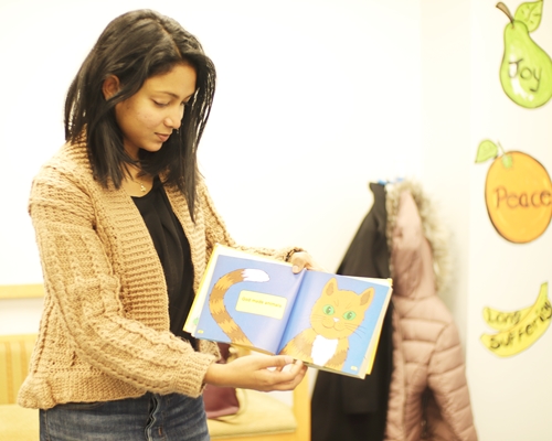 A lady standing and looking at a picture book that she has opened in front of her and showing the picture in the book