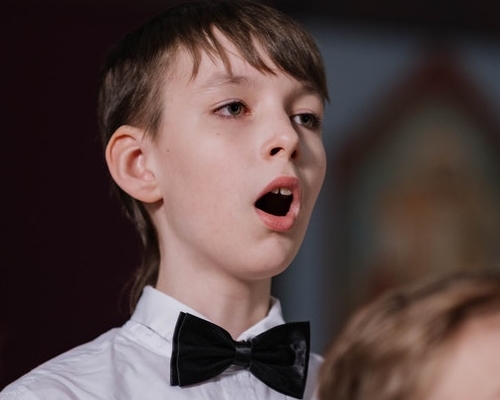 Boy in black bow tie has mouth open to speak or sing