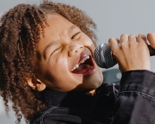 Little girl wearing a black jacket and holding and singing into the microphone