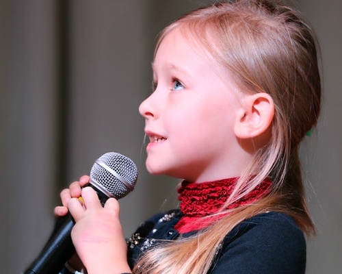 Little girl wearing a red scarf and holding a microphone looking up and smiling