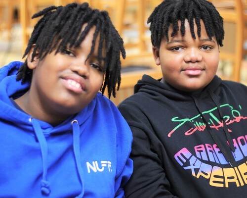 A two young boys sitting down beside each other and smiling at the camera