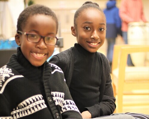 A young boy and girl sitting down beside each other and smiling at the camera