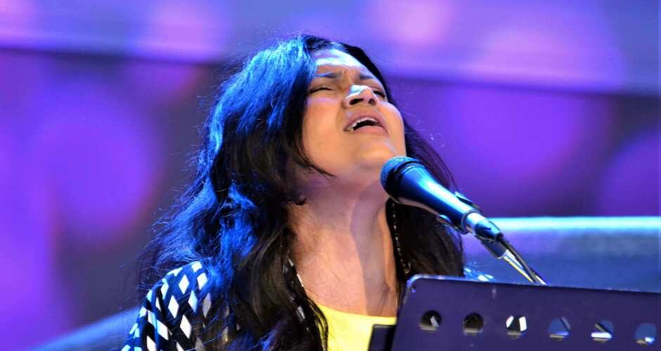 Woman at a piano in front of a mic with head up