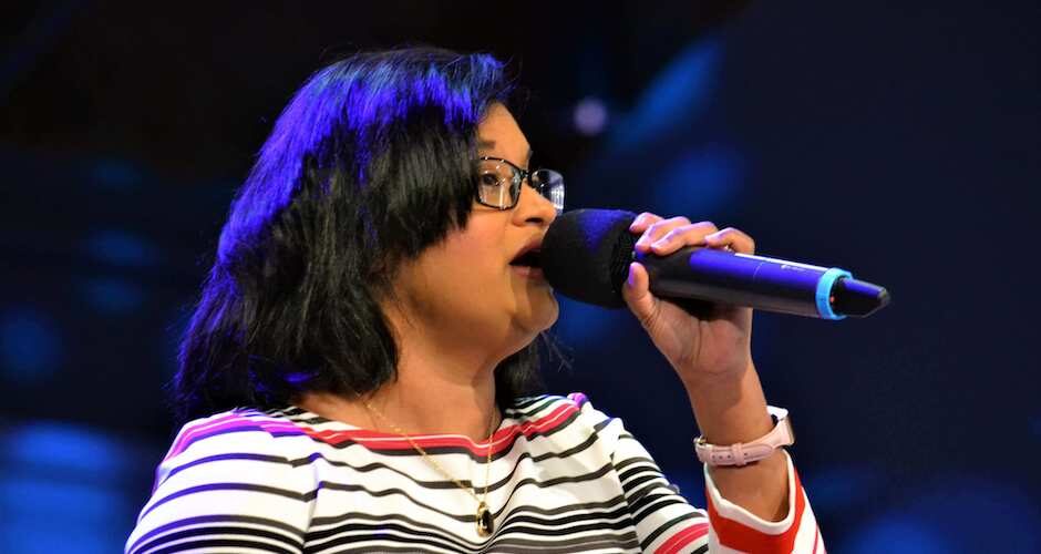 Woman with glasses holding a mic and singing
