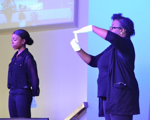 Lady with white gloves using both hands to make a sign language symbol